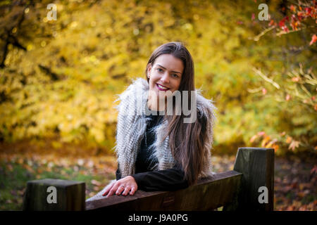 Signora giovane godendo di caldi colori autunnali nei boschi circondate da acero canadese lasciare gli alberi e il giapponese acer alberi di acero, sfumature di rosso, arancione Foto Stock