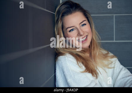 Piuttosto giovane donna bionda con un bel sorriso sincero Pendente ritornare nell'angolo su un grigio parete piastrellata con bracci ripiegati guardando al lato con copia s Foto Stock