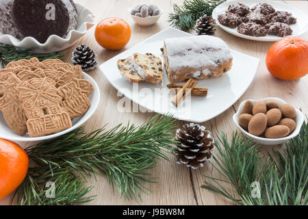 Disposizione di panpepato, biscotti speziati e Mini Christstollen sulla luce sullo sfondo di legno circondato da decorazioni natalizie. Foto Stock