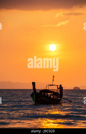 Silhouette di un pescatore su una barca lungo al tramonto off Railay Beach Thailandia Foto Stock