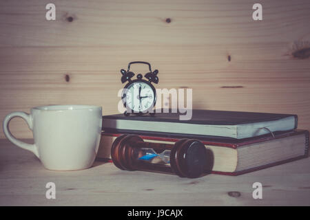 Tazza di caffè clessidra orologio sveglia con libro sulla scrivania in legno Foto Stock