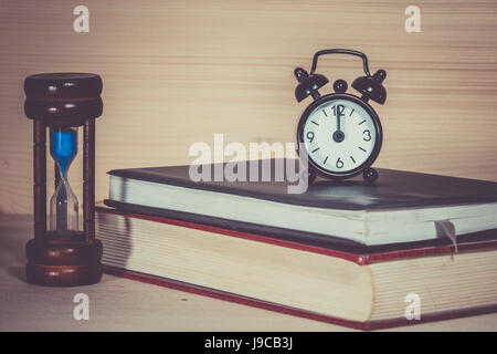 Orologio sveglia a clessidra con libro sulla scrivania in legno Foto Stock