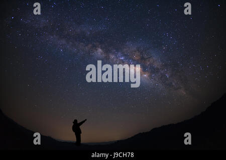 Un uomo è in piedi accanto alla via lattea puntando su una stella luminosa, una lunga esposizione fotografia, con grano. Foto Stock