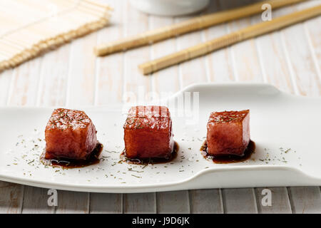 Tonno sashimi immerso in salsa di soia, spessa sale e aneto con bacchette di bambù e mat. Pesce crudo in tradizionale stile Giapponese. L'immagine orizzontale. Foto Stock