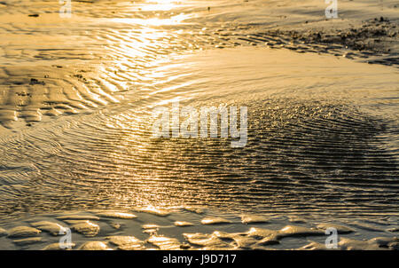 Increspature di acqua a bassa marea su una spiaggia di sabbia con la luce del sole che riflette nell'acqua di mare. Foto Stock