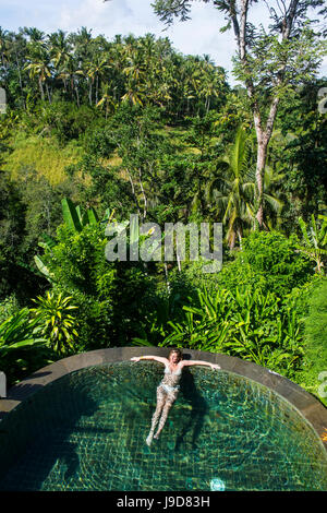 Donna godendo di un traboccare piscina al di sopra di una valle nel Kamandalu Resort Ubud, Ubud, Bali, Indonesia, Asia sud-orientale, Asia