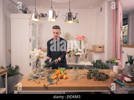 Un giovane uomo adulto, fioraio, disponendo dei fiori, negozio di fiori in ambienti interni Foto Stock