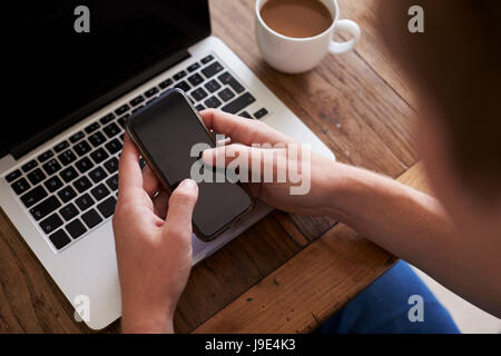 Uomo di inviare un messaggio di testo sul telefono cellulare mentre utilizzando Laptop Foto Stock