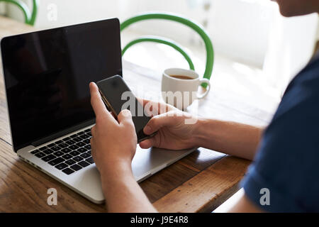 Uomo di inviare un messaggio di testo sul telefono cellulare mentre utilizzando Laptop Foto Stock