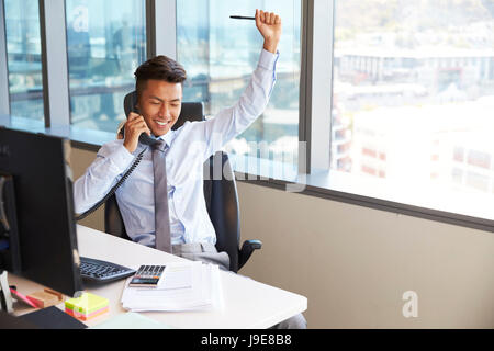 Celebrando imprenditore rendendo chiamata alla scrivania in ufficio Foto Stock