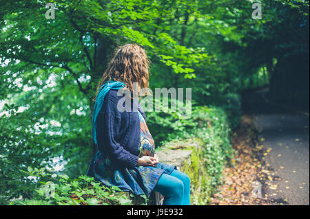 Una giovane donna incinta è seduta sul ciglio della strada in una foresta Foto Stock