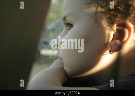 Bambina guardando fuori dalla finestra. Bambini in viaggio. Bambino da solo. In attesa di qualcuno o manca qualcuno. Foto Stock