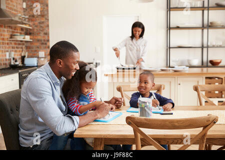 Padre e figli disegno a tavola come madre prepara la cena Foto Stock