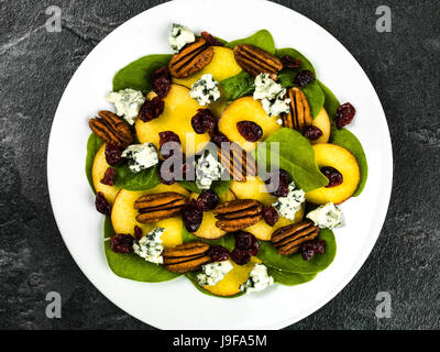 Pesche fresche e insalata di spinaci con noci pecan e formaggio blu contro un nero ardesia sfondo Foto Stock