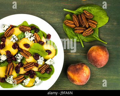 Pesche fresche e insalata di spinaci con noci pecan e formaggio blu contro uno sfondo verde Foto Stock