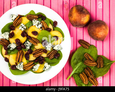 Pesche fresche e insalata di spinaci con noci pecan e formaggio blu contro un sfondo rosa Foto Stock