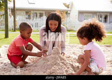 Docente presso la Scuola Montessori a giocare con i bambini nella buca di sabbia Foto Stock