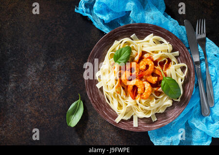 Spaghetti con salsa di pomodoro e gamberi in una piastra sul buio, di calcestruzzo o di pietra ardesia sfondo. Vista da sopra con copia spazio. Foto Stock