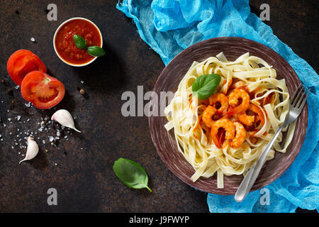 Spaghetti con salsa di pomodoro e gamberi in una piastra sul buio, di calcestruzzo o di pietra ardesia sfondo. Vista da sopra con copia spazio. Foto Stock