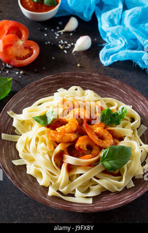 Spaghetti con salsa di pomodoro e gamberi in una piastra sul buio, di calcestruzzo o di pietra ardesia sfondo. Vista da sopra con copia spazio. Foto Stock