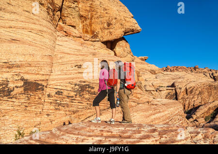 Coppia con arrampicata su roccia marcia ammirare luce dorata al tramonto un tRed Rock Canyon National Conservation Area, che si trova a circa 20 miglia dal Las Vegas Foto Stock