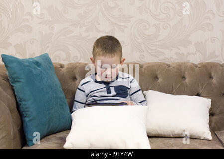 Ragazzo seduto sul divano e guardando il tablet Foto Stock