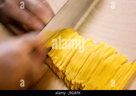 Tagliatelle. Tradizione artigianale italiana la pasta fresca, il sottile nastro sagomato. Il momento del taglio nel procedimento di preparazione. Foto Stock