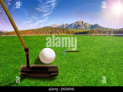 Il Golfer usando un putter club di colpire una pallina da golf su un bellissimo campo da golf con laghi e del paesaggio di montagna nelle prime ore del mattino. La deliberata lens flare. Foto Stock