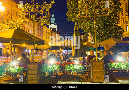 LEOPOLI, UCRAINA - 16 MAGGIO 2017: Vista notturna del caffè all'aperto nella piazza del mercato (Ploshcha Rynok) con fiori in pentole, alberi in fiore e luci accese Foto Stock