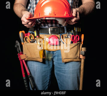 Dettaglio del tuttofare con cuoio toolsbelt e strumenti su sfondo scuro holding casco Foto Stock