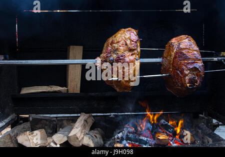 Gran parte di carne cotti su una griglia di ruotare su un fuoco aperto. Grigliate di carne bistecche preparate all'esterno. Affumicato vecchio alla griglia prosciutto di Praga. Foto Stock