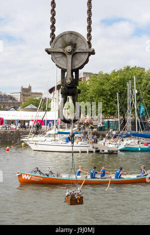 Bristol, Inghilterra - Luglio 17, 2016: un vintage dockside gru solleva una scatola di giocattoli imbottiti mentre una squadra di canottaggio passa come parte di dimostrazioni durante il Foto Stock