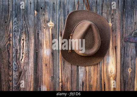 Brown Lana Feltro il cappello da cowboy con fascia di cuoio appeso a spiovente parete in legno del vecchio fienile Foto Stock