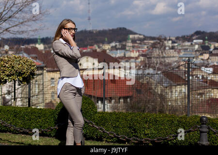 Snella bionda parlando al telefono. Donna che indossa tuta e occhiali. Posizione di parcheggio. Foto Stock