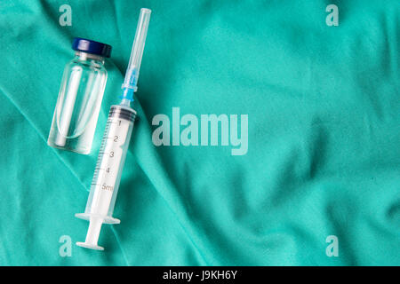 Siringa medica e fiale giacente sull'ospedale sfondo verde. Lo sfondo può essere una parte di tessili di un medico o un infermiere uniforme di lavoro Foto Stock