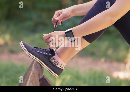Close up shoot di legatura femmina lacci delle scarpe e indossando watchband touchscreen smart guarda con schermo vuoto all'esterno. Uno stile di vita sano e nuovo technolog Foto Stock
