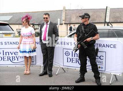 Racegoers guardare come un agente di polizia armato sorge in guardia sul Signore giorno durante il 2017 Investec Epsom Derby Festival presso la Epsom Racecourse, Epsom. Foto Stock