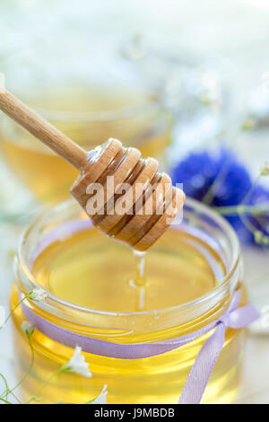 Il miele in vasetti di vetro e la tazza di tè bianco con fiori di primavera e di Fiordaliso sul davanzale. Profondità di campo. Foto Stock