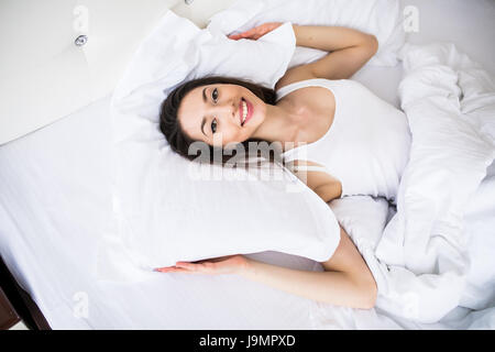 Bella giornata sognatore. Vista superiore della bella giovane donna tenendo le mani dietro il cuscino mentre giaceva a letto e sorridente Foto Stock