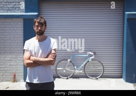 Ritratto del dipendente in piedi con la bicicletta è parcheggiata da officina in sottofondo durante la giornata di sole Foto Stock