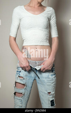 Giovani caucasici slim donna che indossa breve top lavorati a maglia con le mani tagliate di abbassamento jeans blu, rivelando mutandina top, addome e tatuaggio. Huddersfield, Regno Unito Foto Stock