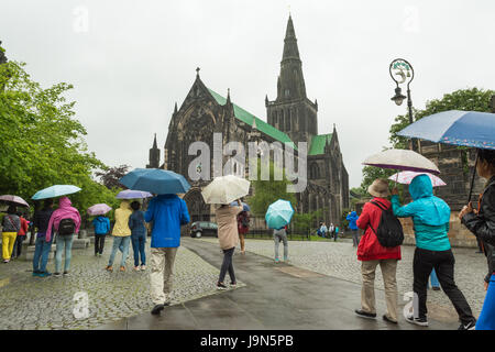 Pioggia di Glasgow - turisti asiatici con ombrelloni colorati al di fuori la cattedrale di Glasgow, Scotland, Regno Unito Foto Stock