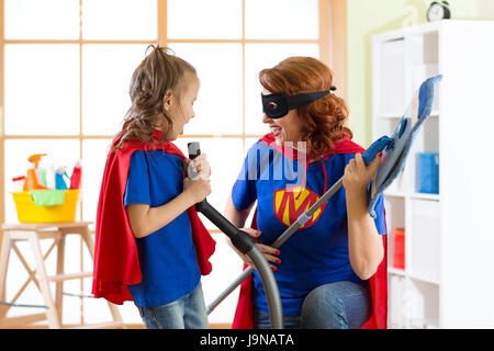 Donna felice con kid pulizia camera e hanno un divertimento. La madre e il bambino ragazza giocare insieme. La famiglia in costumi di supereroi. Foto Stock