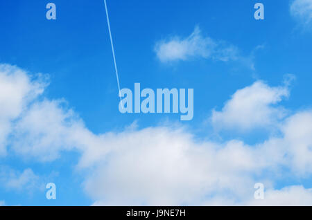 Aeroplano vola in nuvole bianche in un cielo blu e lasciando il sentiero Foto Stock