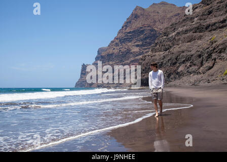 Gran Canaria, spiaggia Playa de Guigui nella parte occidentale dell'isola, accessibile solo a piedi o in barca; giovani escursionisti a piedi lungo la linea di galleggiamento Foto Stock