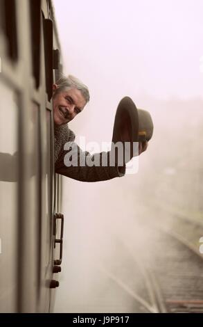 La guerra sulla linea rievocazione storica evento sulla linea di crescione. L'uomo sventolando hat dal movimento del treno finestra, metà Hants Railway, Hampshire REGNO UNITO Foto Stock