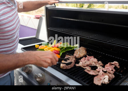 Uomo di bistecca alla brace e diversi tipi di peperone su un grill a gas, close up Foto Stock