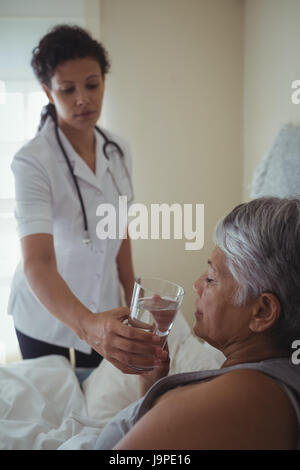 Medico donna dando malati senior donna un bicchiere di acqua sul letto di casa Foto Stock