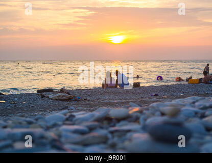 Un giovane e ripiegati a piramide Zen pietre ghiaia sul mare spiaggia al tramonto Foto Stock