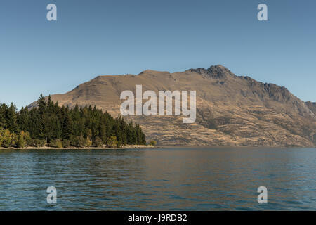 Queenstown, Nuova Zelanda - 15 Marzo 2017: Brown mountain range con picco di Cecil attraverso blu scuro sul lago Wakatipu e downtown, sotto leggero blue sky. Pa Foto Stock